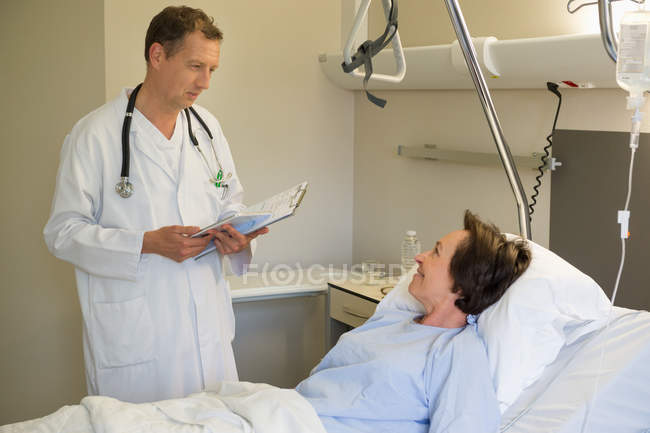 Médico varón hablando con paciente en cama de hospital - foto de stock