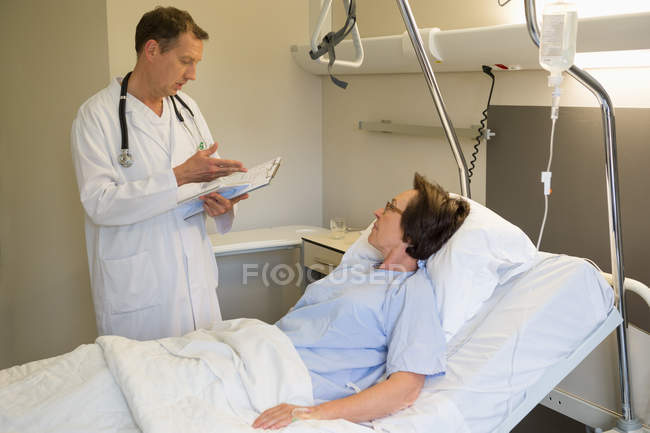 Médico masculino conversando com paciente na cama do hospital — Fotografia de Stock