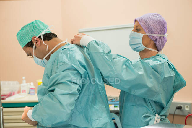 Женщина-хирург помогает хирургу-мужчине надеть защитную одежду — стоковое фото