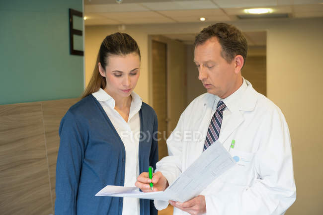 Médico varón discutiendo informe médico con mujer en el hospital - foto de stock