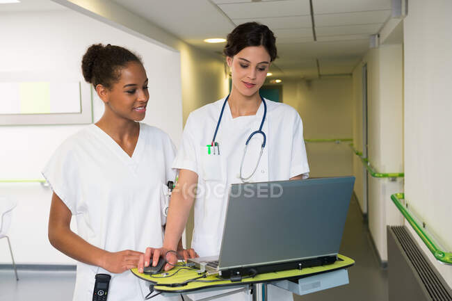 Doctora y enfermera usando laptop en corredor hospitalario - foto de stock