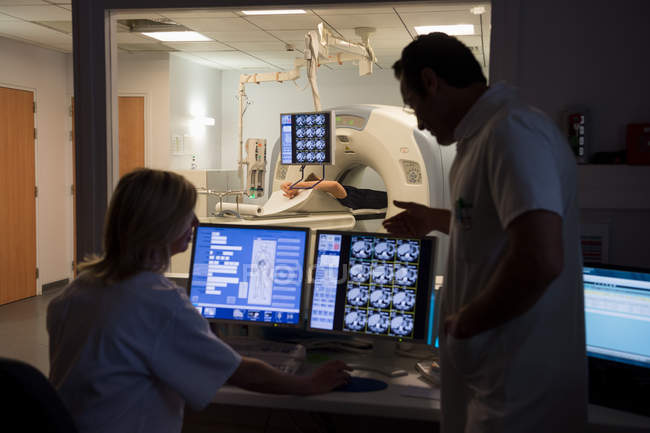 Врачи, изучающие сканирование на компьютере с пациентом на МРТ-сканере в фоновом режиме — стоковое фото