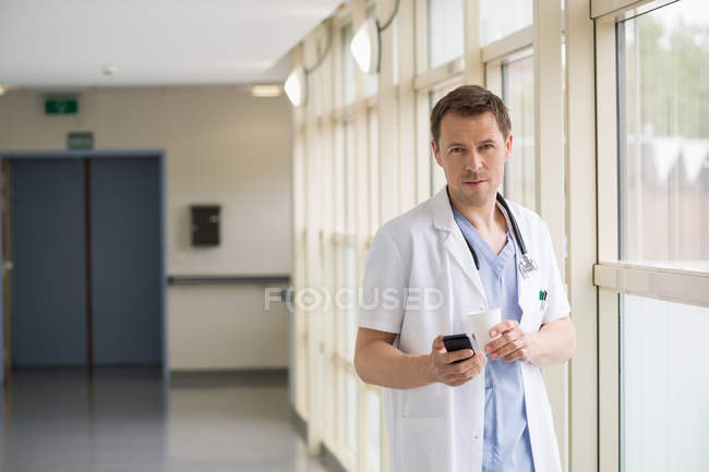 Ritratto del medico maschio che messaggia con il telefono cellulare mentre beve caffè — Foto stock