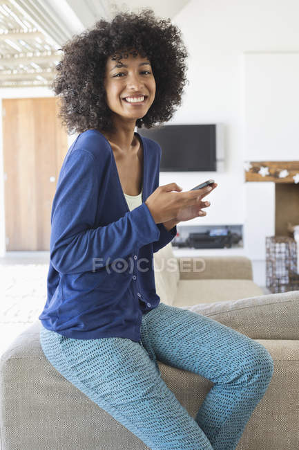 Улыбающаяся женщина с мобильного телефона, опираясь на диван дома — стоковое фото