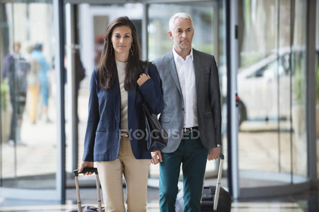 Business couple pulling suitcases in a hotel lobby — Stock Photo