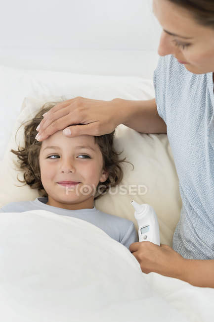 Mulher tocando a testa do filho parecendo doente — Fotografia de Stock