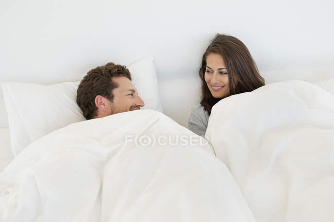 Sorridente coppia a riposo sul letto e guardando l'un l'altro — Foto stock