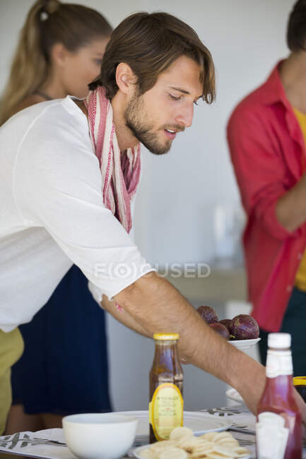 Man arranging a dining table with his friends in the background — Stock Photo