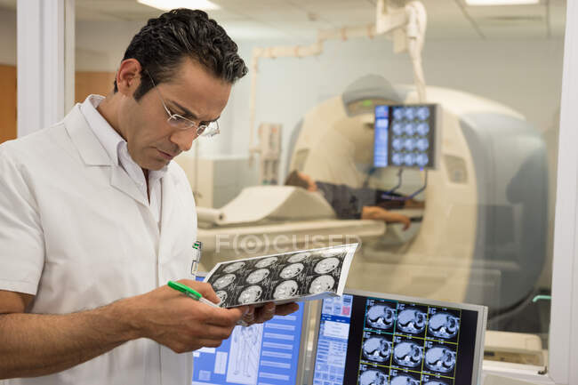 Médico varón examinando informe de resonancia magnética en sala de exploración médica - foto de stock