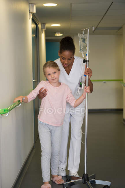 Female nurse helping to a girl patient to walk in hospital corridor — Stock Photo