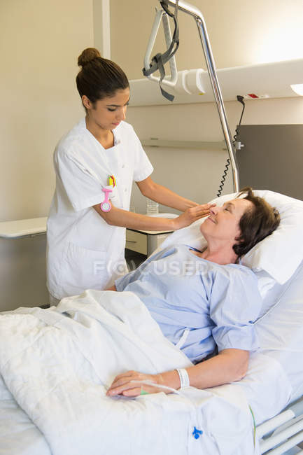 Жіноча медсестра, яка відвідує пацієнта на лікарняному ліжку — стокове фото