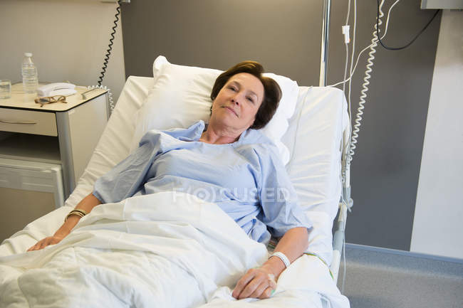 Sonriente mujer madura acostada en la cama del hospital y mirando a la cámara - foto de stock