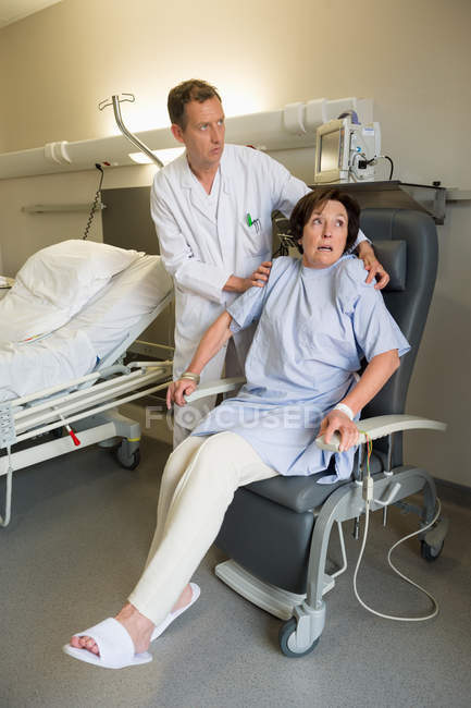 Médico varón ayudando a una paciente sentada en una silla en el hospital - foto de stock
