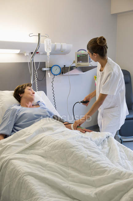 Женщина-медсестра проверяет давление пациента на больничной койке — стоковое фото