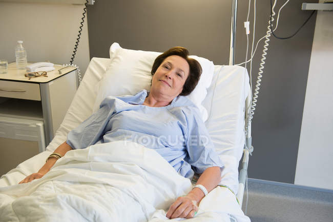 Улыбающаяся взрослая женщина лежит на больничной койке и смотрит в камеру — стоковое фото