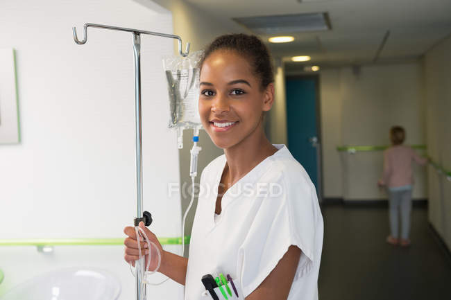 Porträt einer Krankenschwester, die einen Tropfständer hält und im Krankenhaus lächelt — Stockfoto
