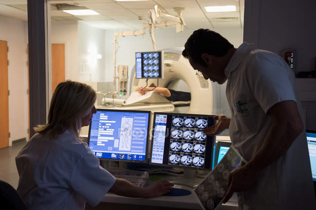 Médicos examinando a varredura no computador com o paciente no scanner de ressonância magnética em segundo plano — Fotografia de Stock