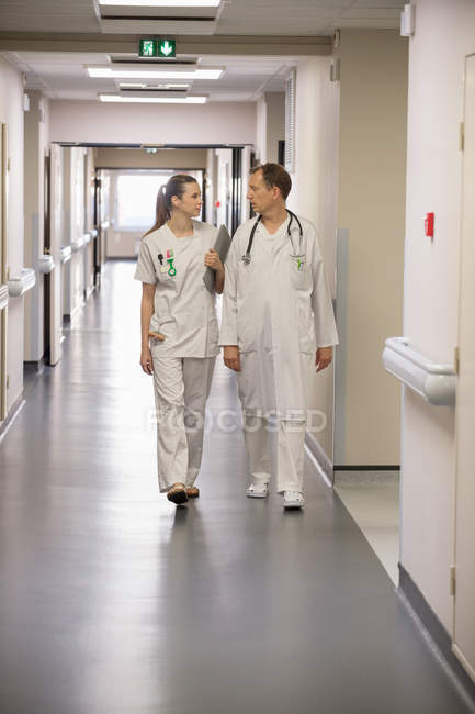 Médico y enfermera caminando por el pasillo de un hospital - foto de stock