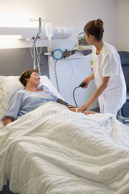 Female nurse checking patient blood pressure on hospital bed — Stock Photo