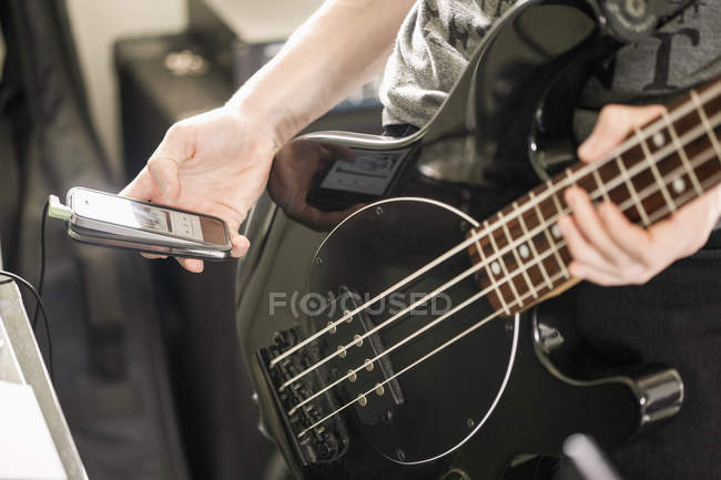 Крупный план мальчика-подростка, играющего на гитаре и использующего мобильный телефон — стоковое фото