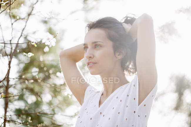 Портрет улыбающейся женщины, трогающей волосы в парке и отводящей взгляд — стоковое фото