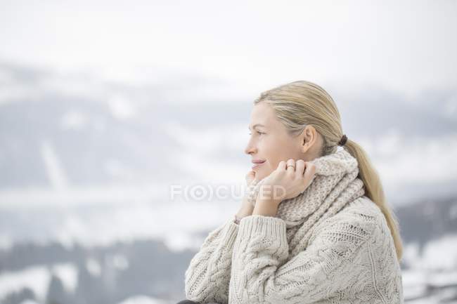 Retrato de mujer madura sonriente sonriendo en suéter cálido y acogedor posando en montañas nevadas - foto de stock