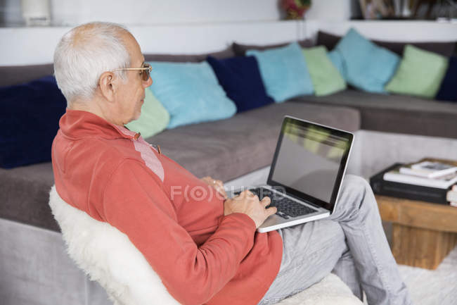 Расслабленный пожилой человек с помощью ноутбука на стуле — стоковое фото
