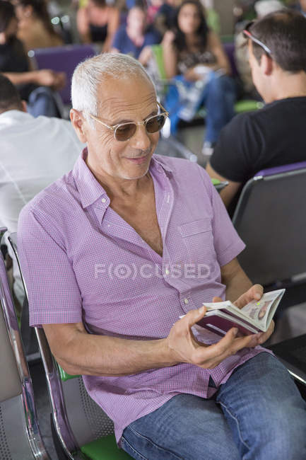 Senior schaut sich Pass in Flughafen-Wartehalle an — Stockfoto
