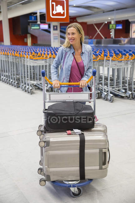 Lächelnde blonde Frau mit Gepäck am Flughafen — Stockfoto