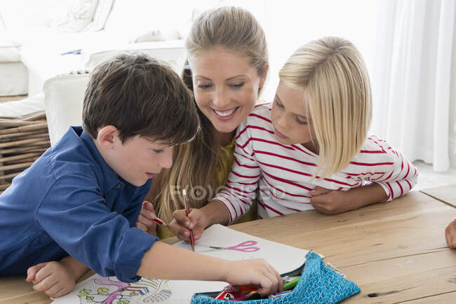 Madre e hijos haciendo la tarea en la mesa - foto de stock