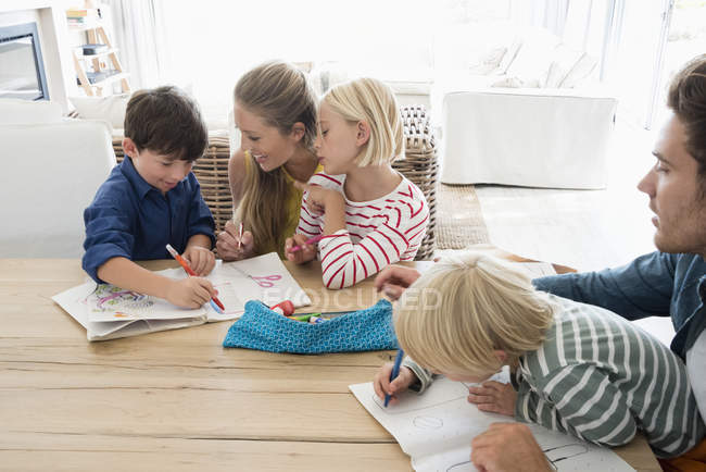 Родители и дети делают домашнее задание за деревянным столом дома — стоковое фото