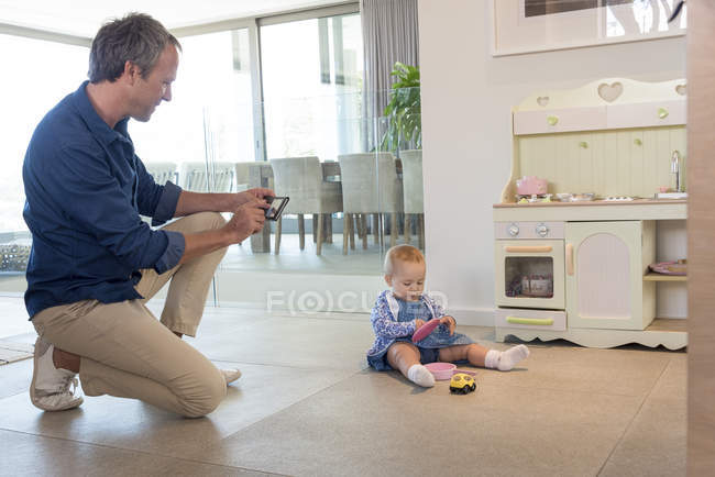 Homme mûr prenant des photos de bébé fille jouer avec des jouets — Photo de stock
