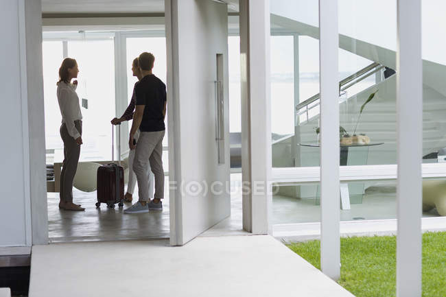 Mujer hablando con amigos con maleta en casa - foto de stock