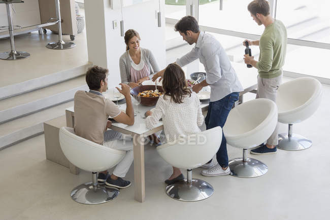 Amigos felices comiendo en la mesa de comedor - foto de stock