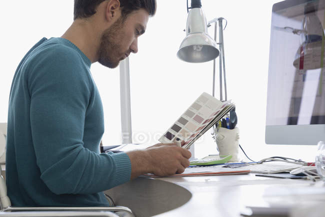Young male designer looking at color swatch in office — Stock Photo