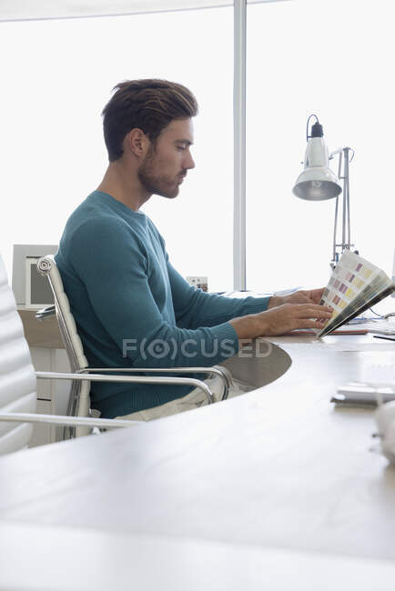 Молодой дизайнер смотрит на цветные образцы в офисе — стоковое фото