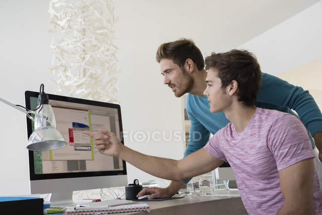 Dos jóvenes empresarios trabajando juntos en un ordenador en una oficina - foto de stock