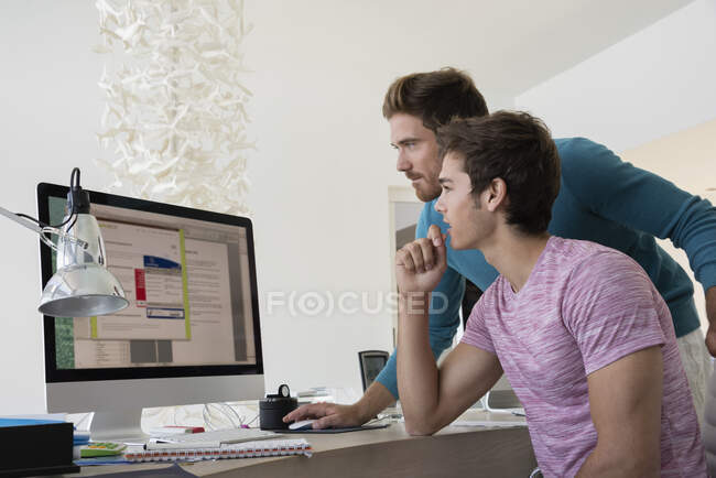 Два молодых бизнесмена, работающих вместе за компьютером в офисе — стоковое фото