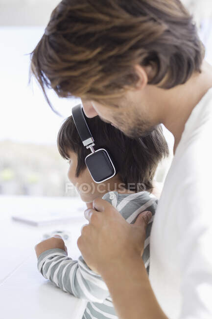 Niño escuchando música con auriculares con padre - foto de stock
