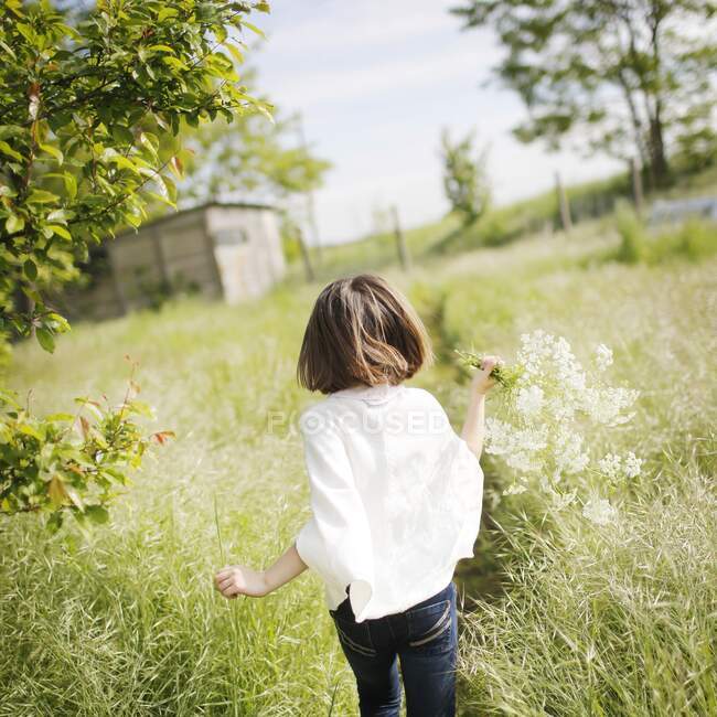 Vue arrière d'une petite fille courant à la campagne avec un bouquet de fleurs à la main — Photo de stock