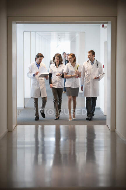 Cuatro doctores caminando por el pasillo de un hospital - foto de stock