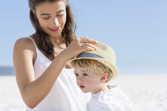 Mujer poniendo sombrero en cabeza de bebé en la playa - foto de stock