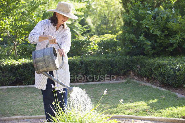 Frau mit Strohhut gießt Pflanzen im Sommergarten — Stockfoto