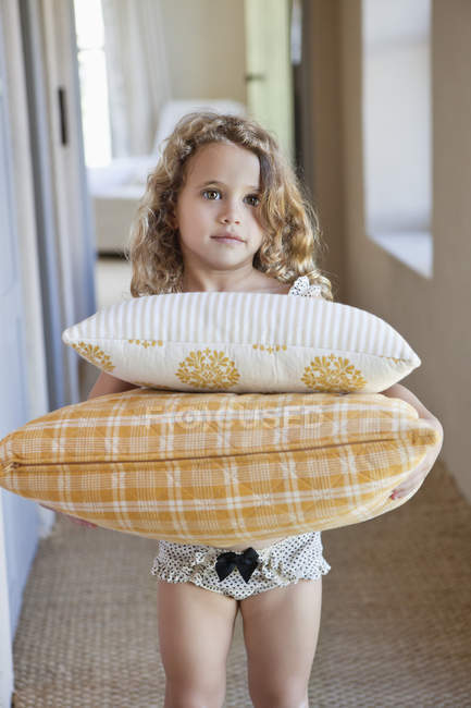 Retrato de linda niña sosteniendo almohadas en casa - foto de stock
