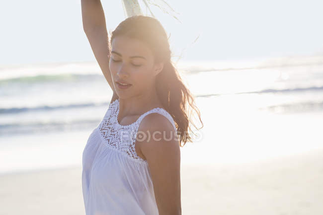 Молода жінка з закритими очима позує на пляжі на задньому світлі — стокове фото