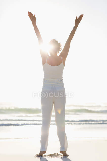 Rear view of woman standing on beach with arms raised — Stock Photo