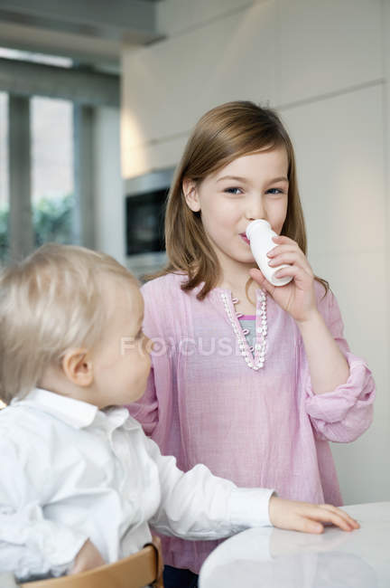 Портрет усміхненої дівчини, що п'є молоко з братом на кухні — стокове фото