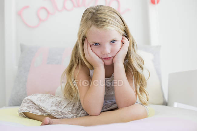 Retrato de una linda niña sentada en la cama con la cabeza en las manos - foto de stock