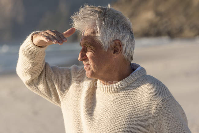 Senior man watching with shielding eyes on beach — Stock Photo