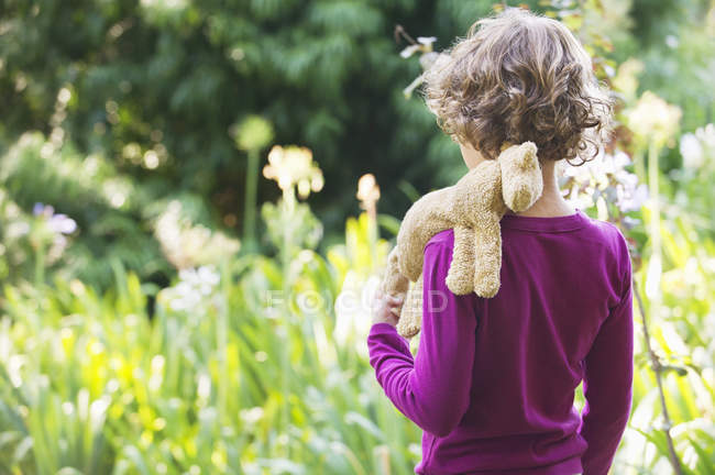 Rear view of little boy standing in meadow with stuffed toy on shoulder — Stock Photo